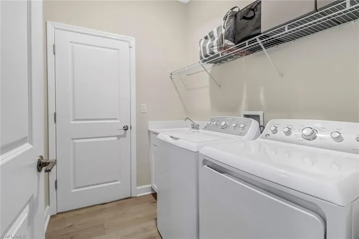 Laundry area with washing machine and clothes dryer, sink, and light hardwood / wood-style floors