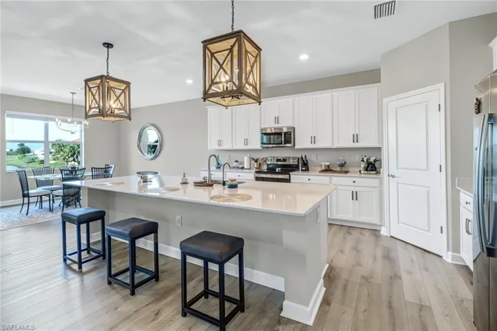 Kitchen with white cabinetry, light hardwood / wood-style floors, hanging light fixtures, appliances with stainless steel finishes, and a center island with sink