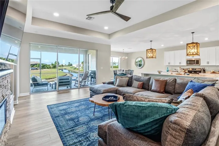 Living room with a stone fireplace, light hardwood / wood-style floors, ceiling fan with notable chandelier, and a raised ceiling