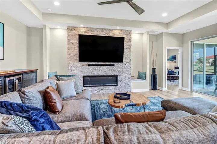 Living room featuring a stone fireplace, light wood-type flooring, and ceiling fan