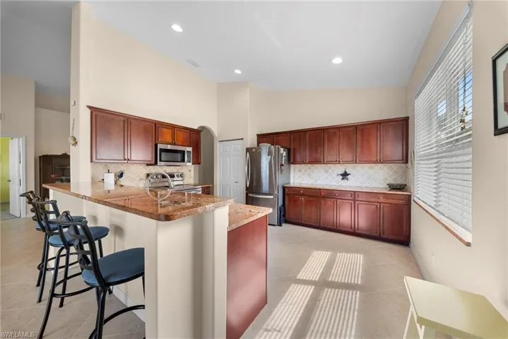 Kitchen featuring a kitchen breakfast bar, arched walkways, stainless steel appliances, light tile patterned flooring, and a peninsula