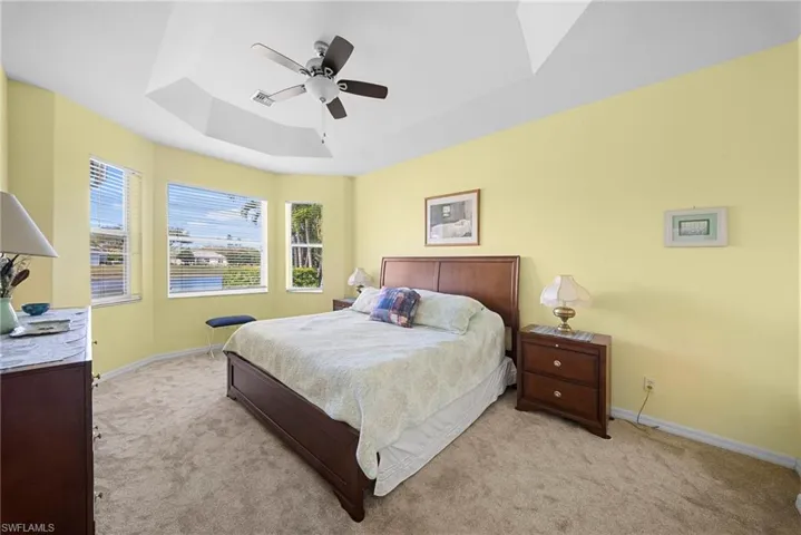 Bedroom featuring light carpet, ceiling fan, and a raised ceiling