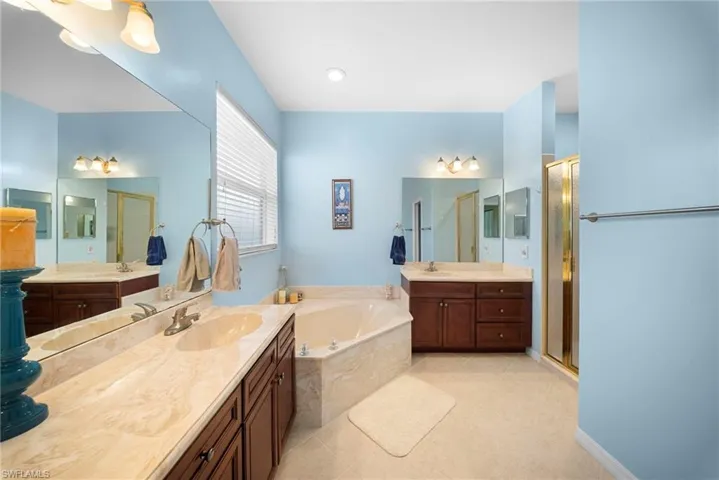 Bathroom featuring two vanities, a garden tub, a shower stall, and light tile patterned flooring