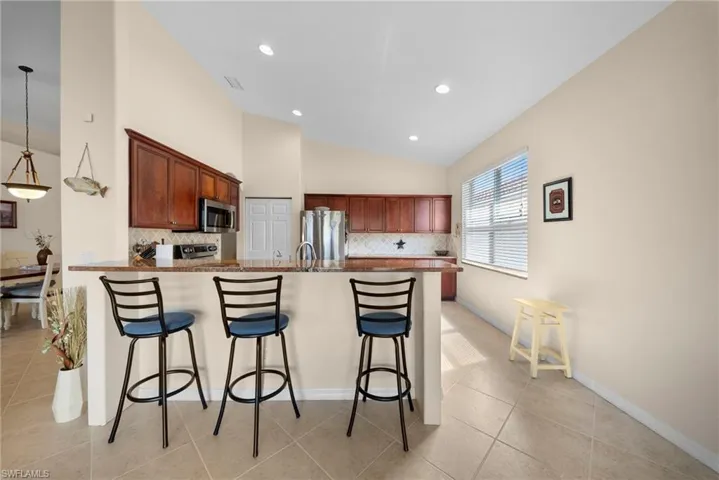 Kitchen featuring a breakfast bar, a peninsula, decorative backsplash, stainless steel appliances, and vaulted ceiling