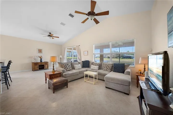 Living room with vaulted ceiling, ceiling fan, and light tile patterned floors