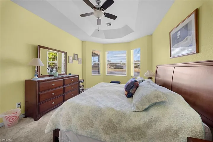 Bedroom featuring a ceiling fan, a raised ceiling, and light carpet