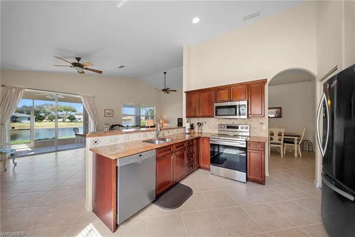 Kitchen with a peninsula, stainless steel appliances, open floor plan, light tile patterned floors, and arched walkways