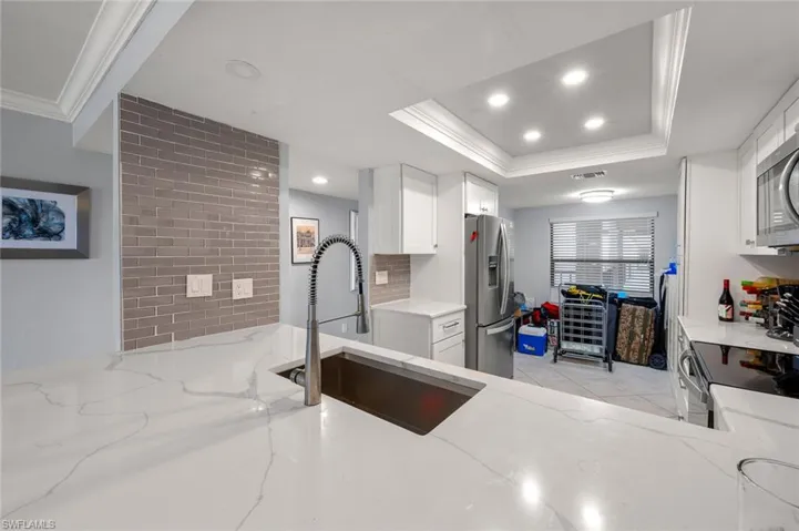 Kitchen with stainless steel appliances, light stone counters, a raised ceiling, ornamental molding, and sink