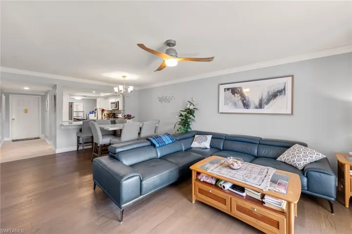 Living room featuring ceiling fan with notable chandelier, crown molding, and wood-type flooring