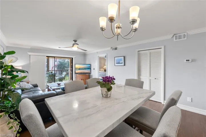 Dining space with ceiling fan with notable chandelier, crown molding, and dark hardwood / wood-style flooring