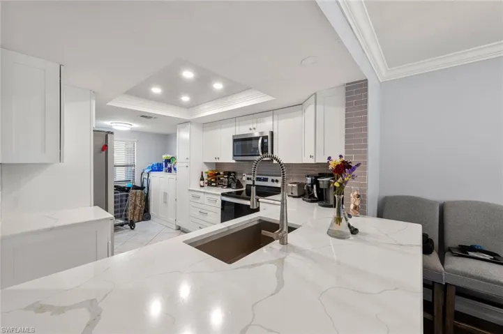 Kitchen with white cabinetry, appliances with stainless steel finishes, light stone countertops, and a raised ceiling