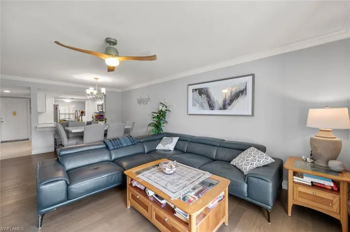 Living room with ceiling fan with notable chandelier, crown molding, and dark wood-type flooring