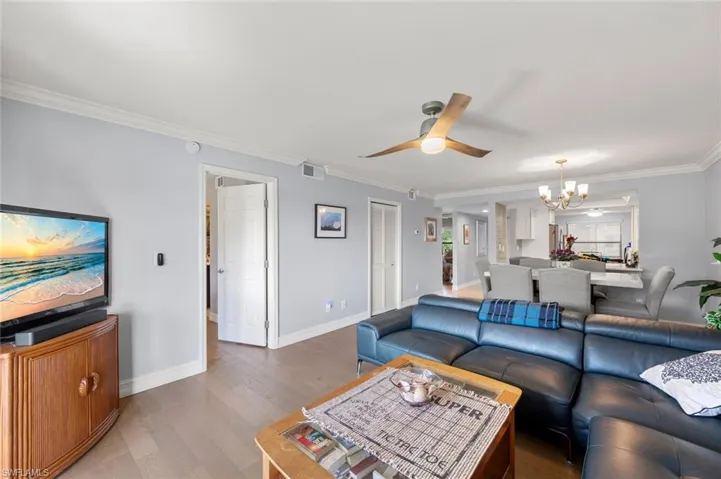 Living room with hardwood / wood-style floors, ceiling fan with notable chandelier, and ornamental molding