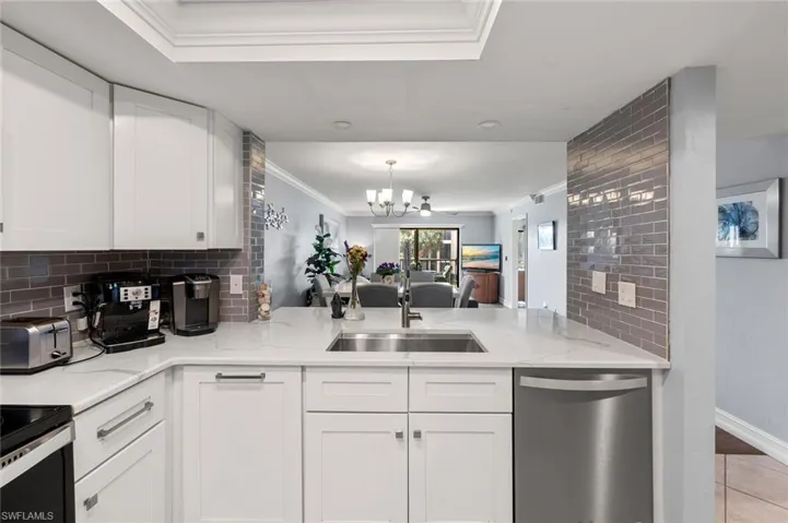 Kitchen with sink, light stone counters, dishwasher, white cabinets, and ornamental molding