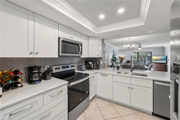 Kitchen with stainless steel appliances, crown molding, a tray ceiling, sink, and white cabinetry