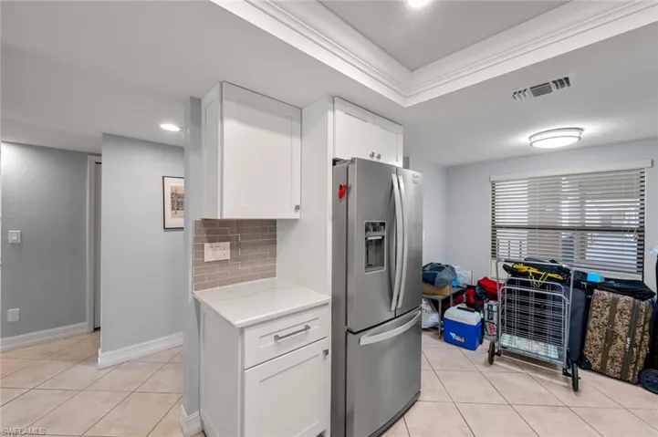 Kitchen with stainless steel refrigerator with ice dispenser, light tile patterned flooring, a tray ceiling, white cabinets, and tasteful backsplash