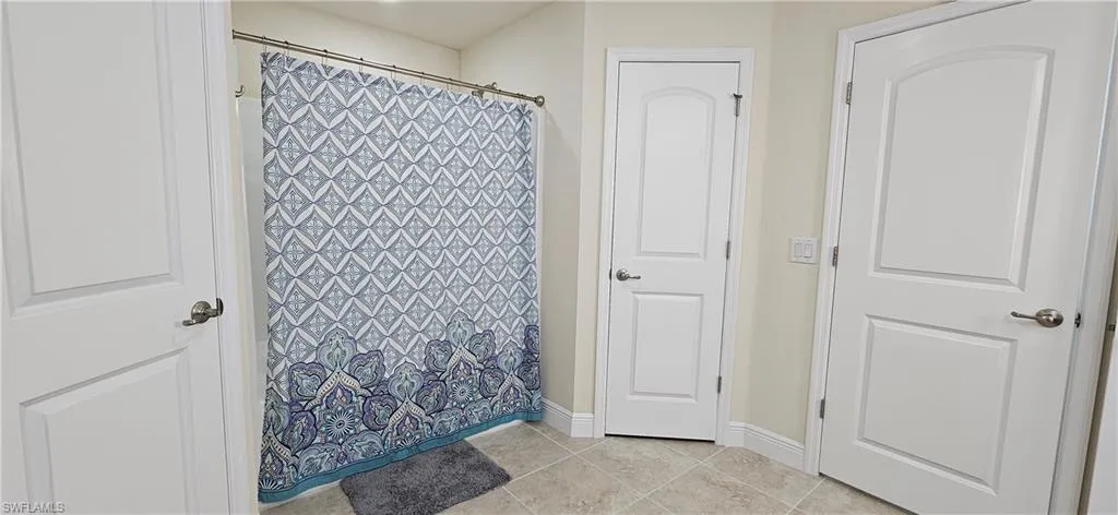 Full bathroom with baseboards, tile patterned flooring, and a shower with shower curtain