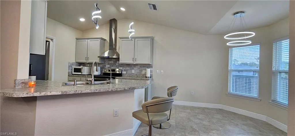 Kitchen featuring white microwave, vaulted ceiling, a kitchen breakfast bar, a sink, and tasteful backsplash