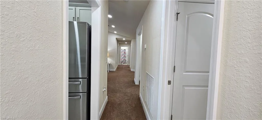Hall featuring a textured wall, dark colored carpet, baseboards, and recessed lighting