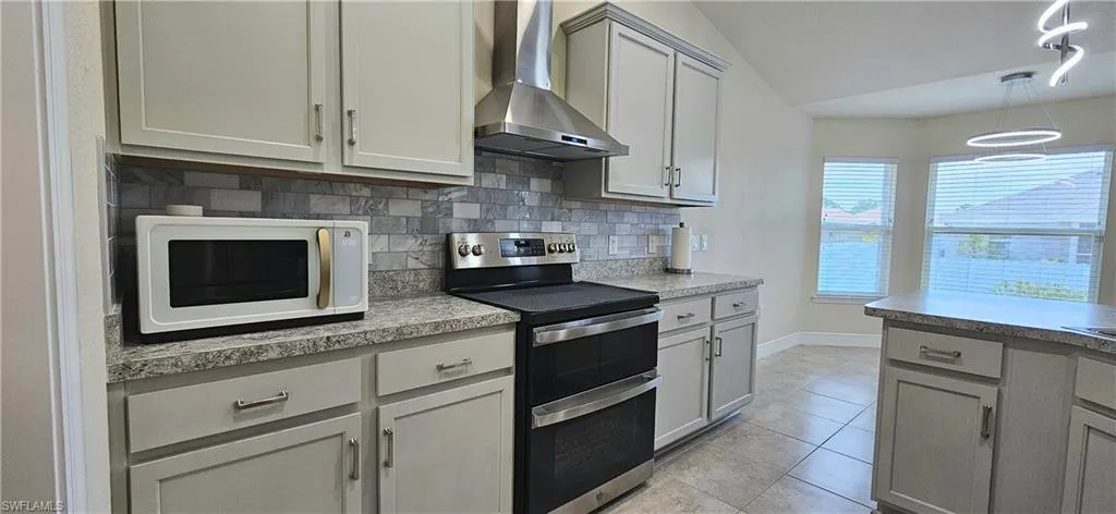 Kitchen featuring double oven range, white microwave, wall chimney range hood, tasteful backsplash, and gray cabinetry