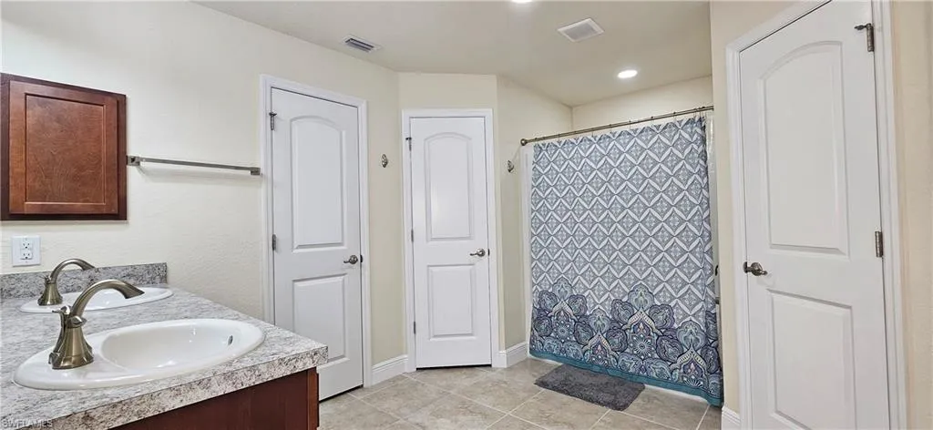 Full bath with tile patterned floors, baseboards, double vanity, and a shower with shower curtain