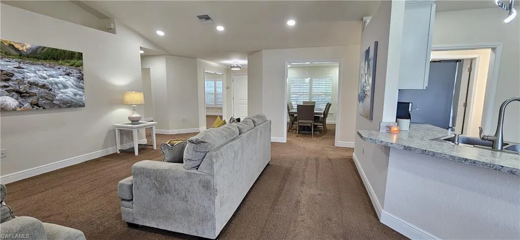 Living room featuring vaulted ceiling, recessed lighting, carpet floors, and baseboards