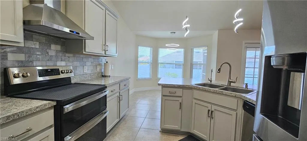 Kitchen with appliances with stainless steel finishes, wall chimney range hood, a sink, light tile patterned floors, and decorative backsplash