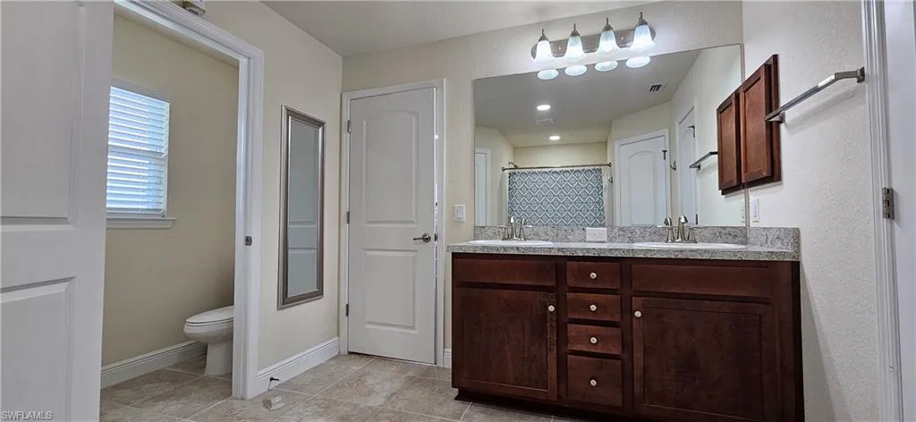 Bathroom featuring tile patterned floors, toilet, double vanity, curtained shower, and baseboards