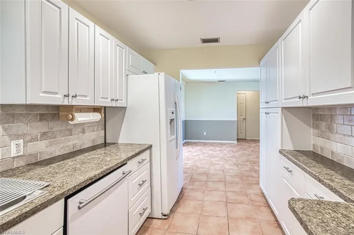 Kitchen featuring white appliances, white cabinetry, decorative backsplash, light tile patterned flooring, and dark stone counters