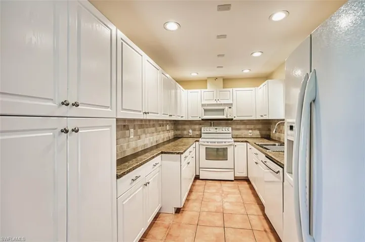 Kitchen featuring white appliances, backsplash, white cabinets, light tile patterned floors, and recessed lighting
