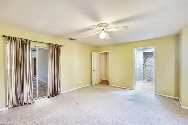 Unfurnished bedroom featuring light carpet, access to exterior, a ceiling fan, and ensuite bath