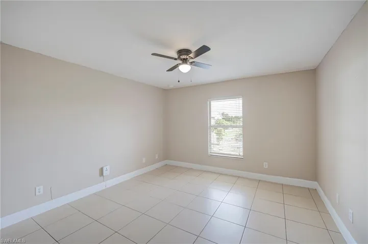 Neutral-toned room featuring a single window with horizontal blinds, a ceiling fan with integrated lighting, and tile flooring
