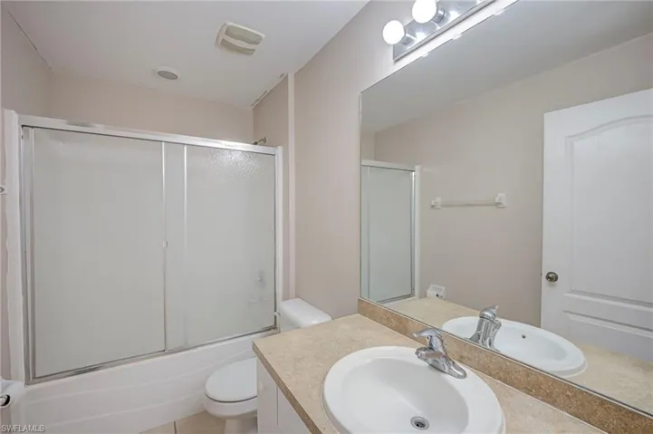 Full bathroom featuring a single vanity with an oval sink, an expansive wall mirror, and a shower-tub combination with sliding frosted glass doors