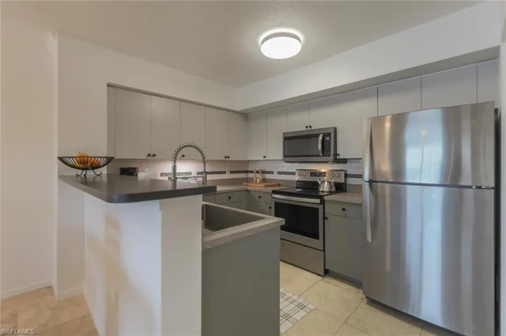 Kitchen with stainless steel appliances, backsplash, kitchen peninsula, and gray cabinetry