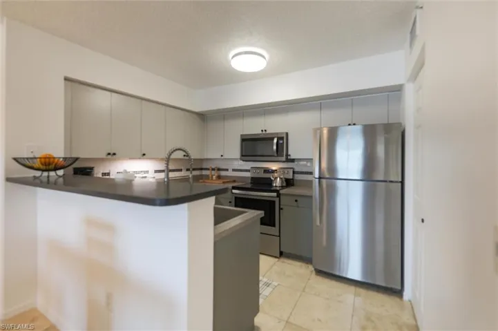 Kitchen with gray cabinets, appliances with stainless steel finishes, kitchen peninsula, and sink