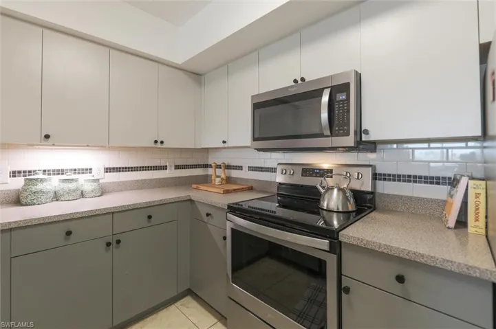 Kitchen featuring gray cabinets, appliances with stainless steel finishes, light tile patterned flooring, and tasteful backsplash