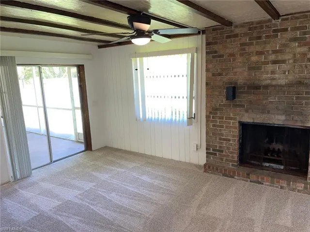 Unfurnished living room featuring carpet flooring, beamed ceiling, a ceiling fan, a fireplace, and wood walls