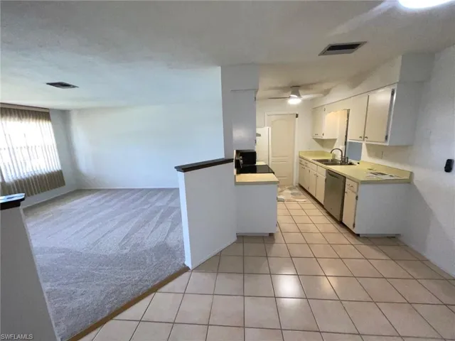 Kitchen featuring stainless steel dishwasher, white cabinets, light countertops, light tile patterned floors, and a ceiling fan