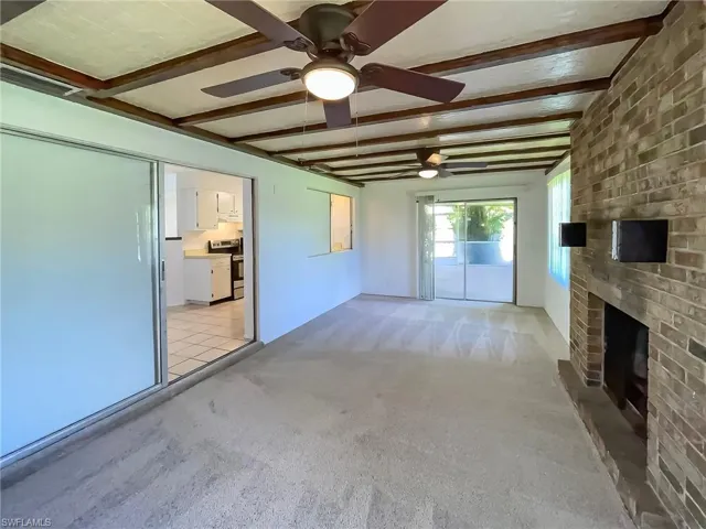 Unfurnished living room with ceiling fan, a fireplace, light carpet, and beam ceiling