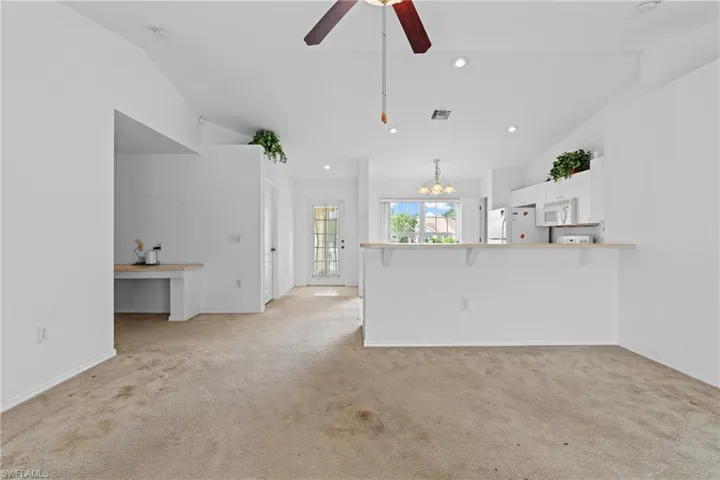 Unfurnished living room with a chandelier, vaulted ceiling, light colored carpet, recessed lighting, and ceiling fan