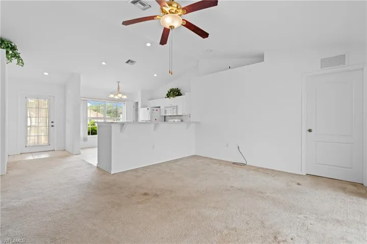 Unfurnished living room with a chandelier, light colored carpet, ceiling fan, high vaulted ceiling, and recessed lighting