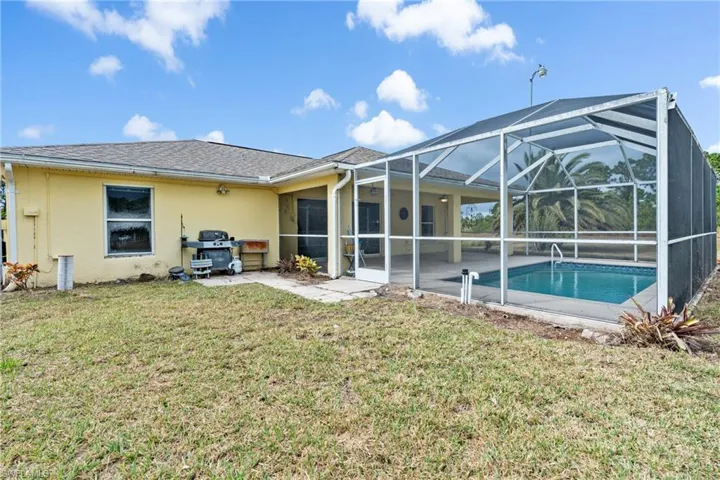 Back of property featuring a sunroom, glass enclosure, a patio area, a lawn, and an outdoor pool
