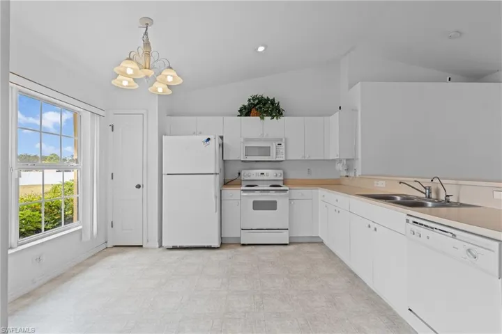 Kitchen with white appliances, light countertops, pendant lighting, vaulted ceiling, and white cabinets