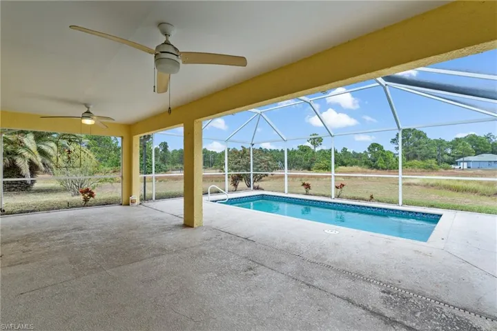 Swimming pool featuring a patio, a lanai, a sunroom, and view of scattered trees