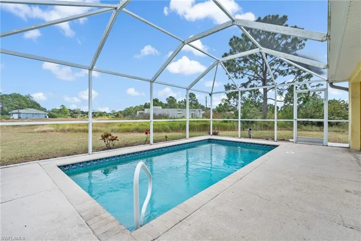 Swimming pool with a sunroom, glass enclosure, a patio area, and a lawn