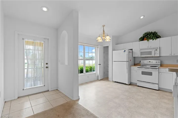 Kitchen featuring white appliances, a chandelier, white cabinets, light countertops, and lofted ceiling