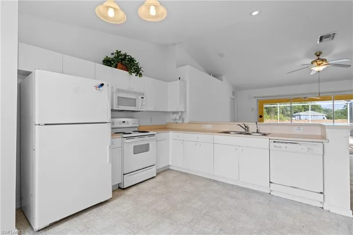 Kitchen featuring white appliances, light floors, light countertops, vaulted ceiling, and white cabinets