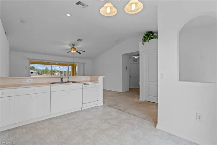 Kitchen with light countertops, white cabinetry, dishwasher, vaulted ceiling, and light floors