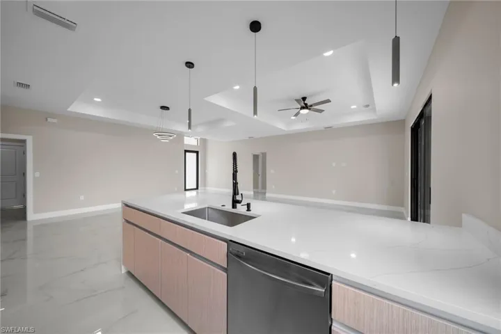 Kitchen featuring decorative light fixtures, open floor plan, a raised ceiling, light brown cabinets, and recessed lighting