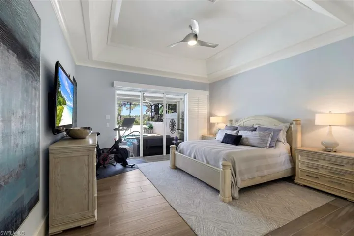Bedroom with a raised ceiling, hardwood / wood-style flooring, access to exterior, and ceiling fan